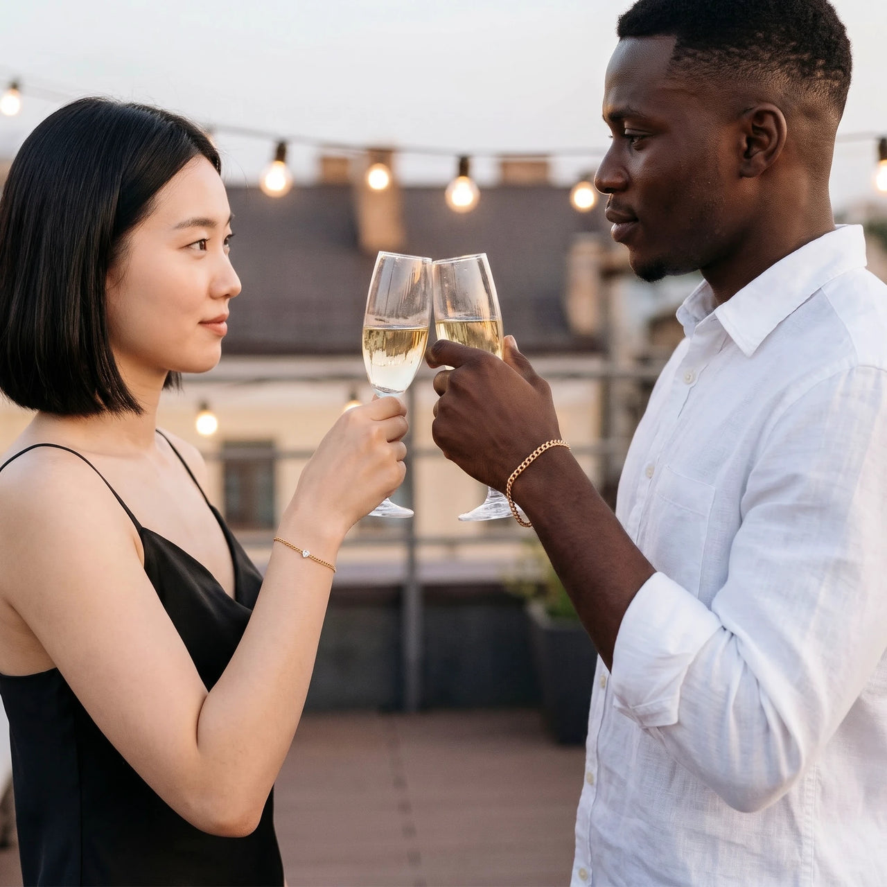 Heart Bond Matching Bracelet Set in Gold — worn by a couple toasting with champagne