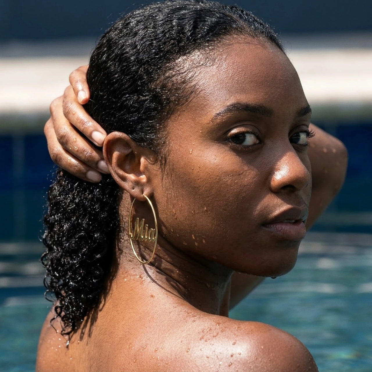 Custom Name Hoop Earrings in Gold worn in a swimming pool, waterproof 304L stainless steel | SKU: name-hoop-gold-30-mm