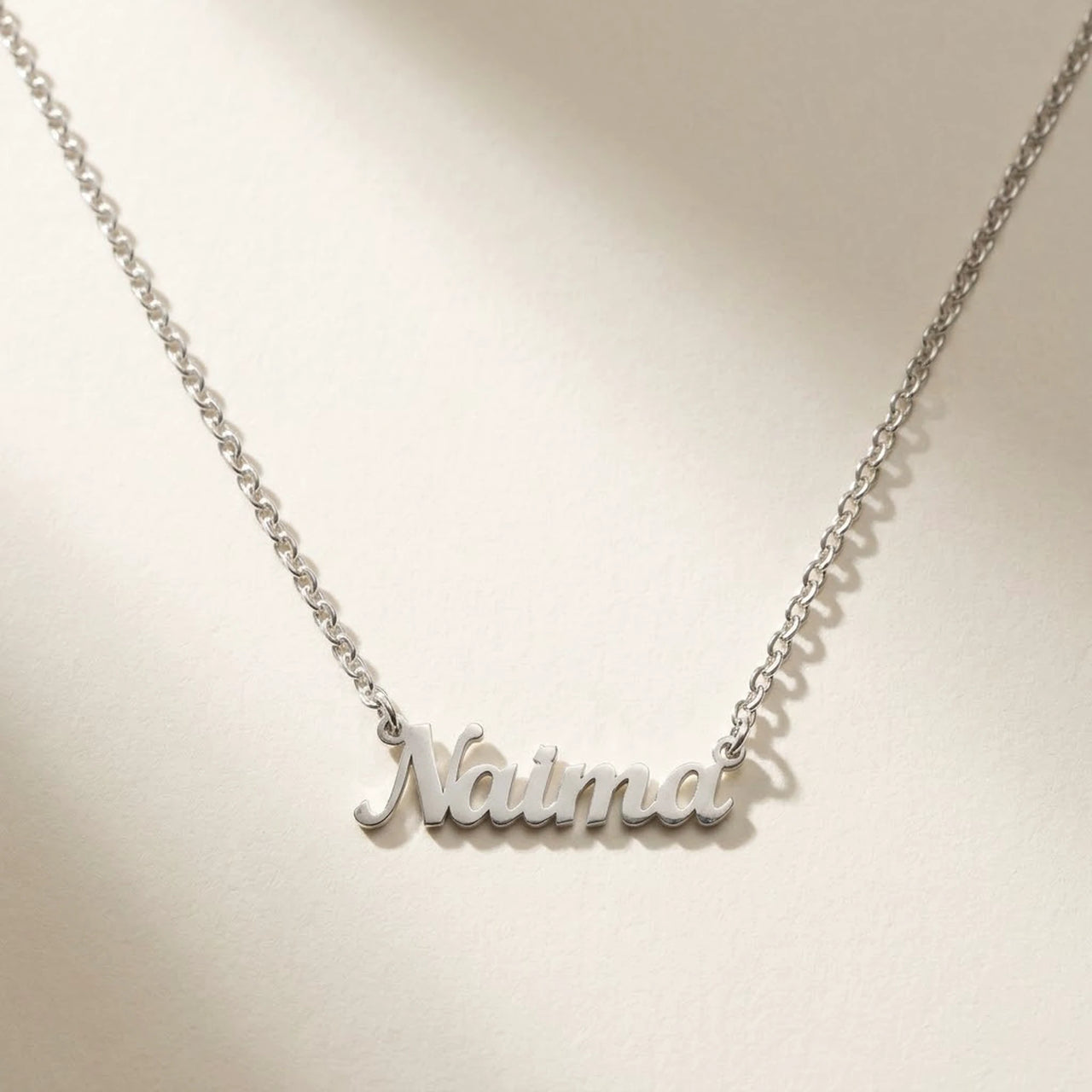 Minimalist Name Necklace in silver laid flat, cursive cut-metal script, the name Naima | SKU: minimalistnn-silver