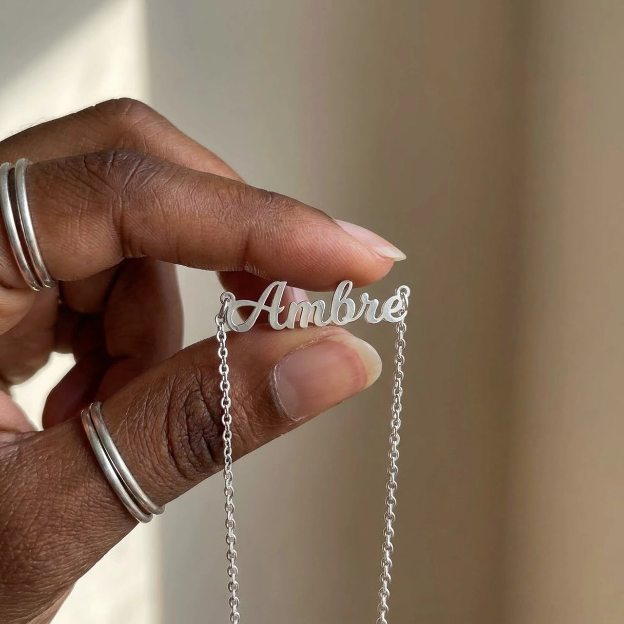 Minimalist Name Necklace in silver pendant held between two fingertips showing its true size, the name Ambre | SKU: minimalistnn-silver